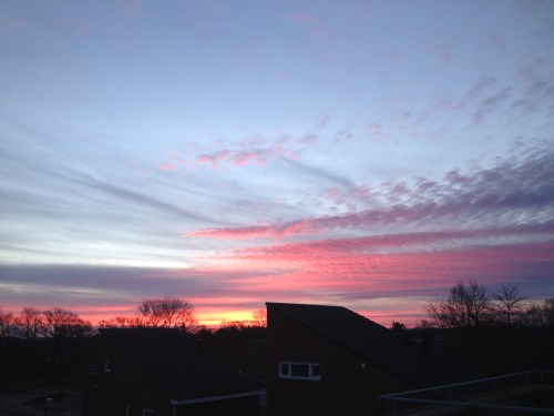 Vuurrod kleurt de hemel terwijl goudgele stralen langzaam over daken kruipt.