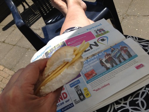 De zondagskrant brengt niet veel nieuws. Ik eet een broodje met mijn benen in de zon.