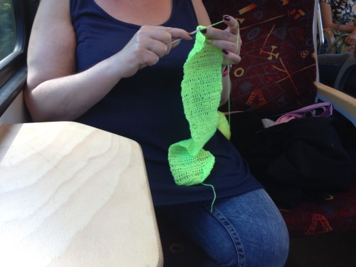 Terwijl verderop een vrouw haar longen er bijna aan 't uithoesten is gaat de dame tegenover mij onverstoorbaar verder met het haken van een gifgroen..euh..ja wat?